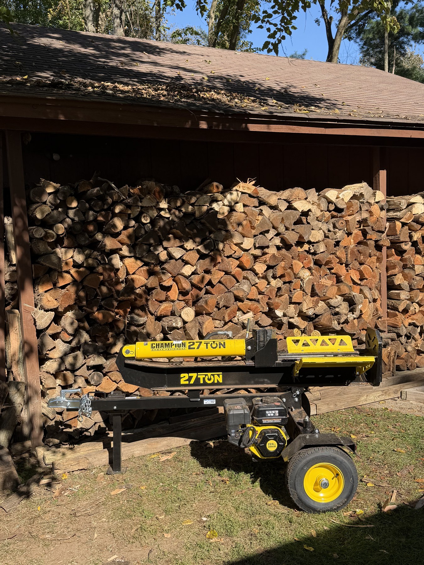 Log splitter in front of a full woodshed at a family wood project